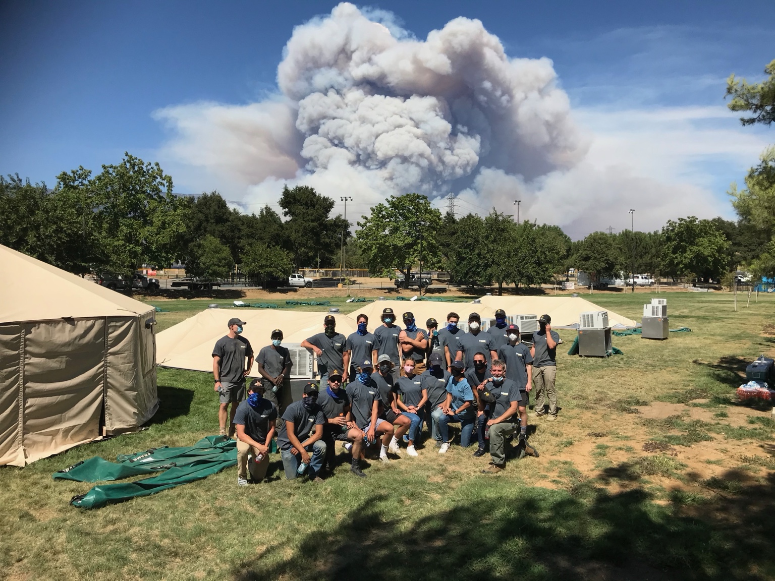 Intents crew at a wildfire support site with a large smoke plume in the distance